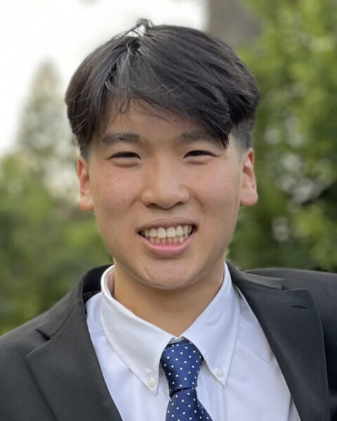 Matthew Chen CLS recipient in a dark suit with blue tie in front of trees.